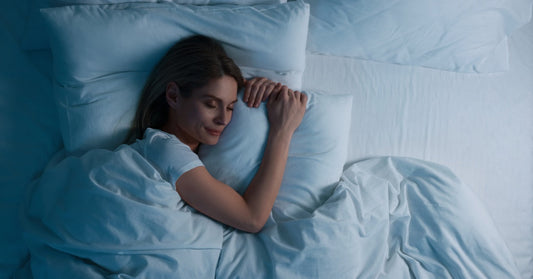 A woman sleeps peacefully with a slight smile on her face under a plush comforter in a bed full of pillows.